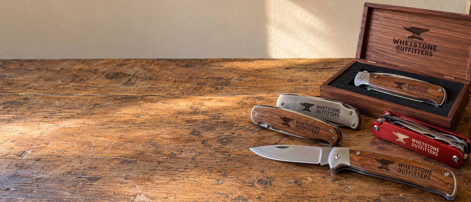 Custom engraved pocket knives resting on a rustic walnut workbench